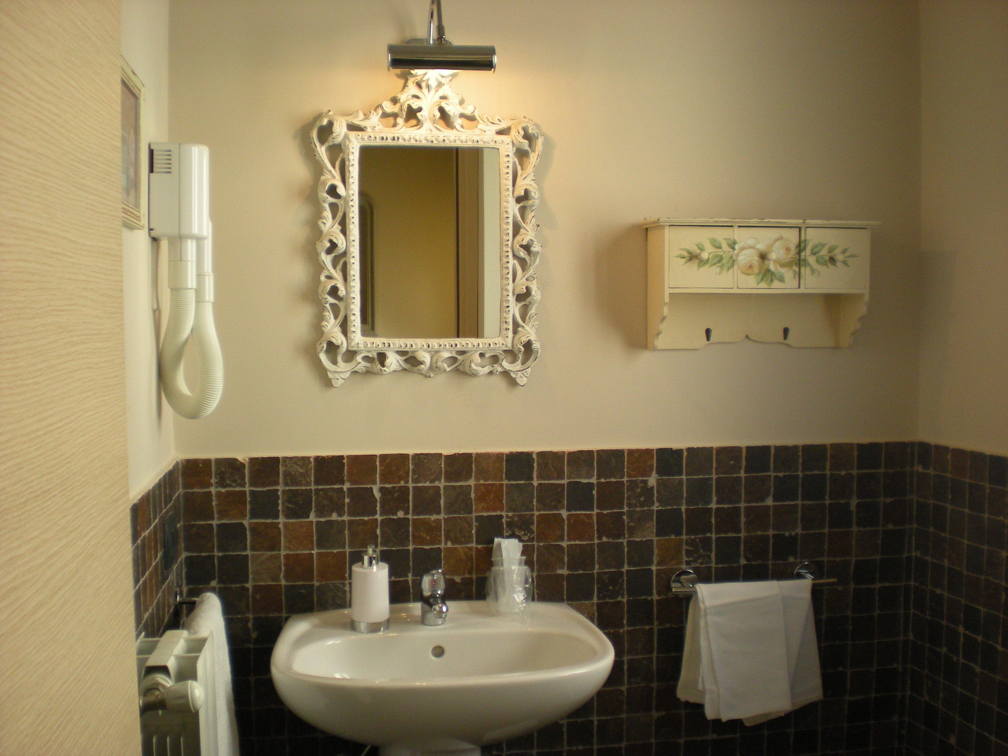 A bathroom with a white sink, a mirror with an ornate frame, a towel hanging on the wall, and a cabinet with floral decorations.