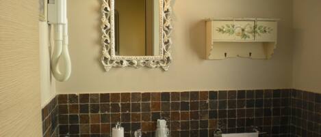 A bathroom with a white sink, a mirror with an ornate frame, a towel hanging on the wall, and a cabinet with floral decorations.