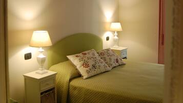 A bedroom with a green bed, two bedside lamps, a nightstand, and a mirror reflecting the room.