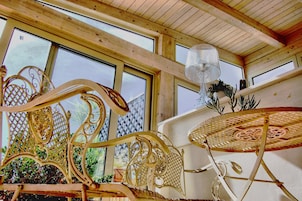 Un interior de madera con ventanas amplias, una silla de metal decorativa y una mesa redonda.