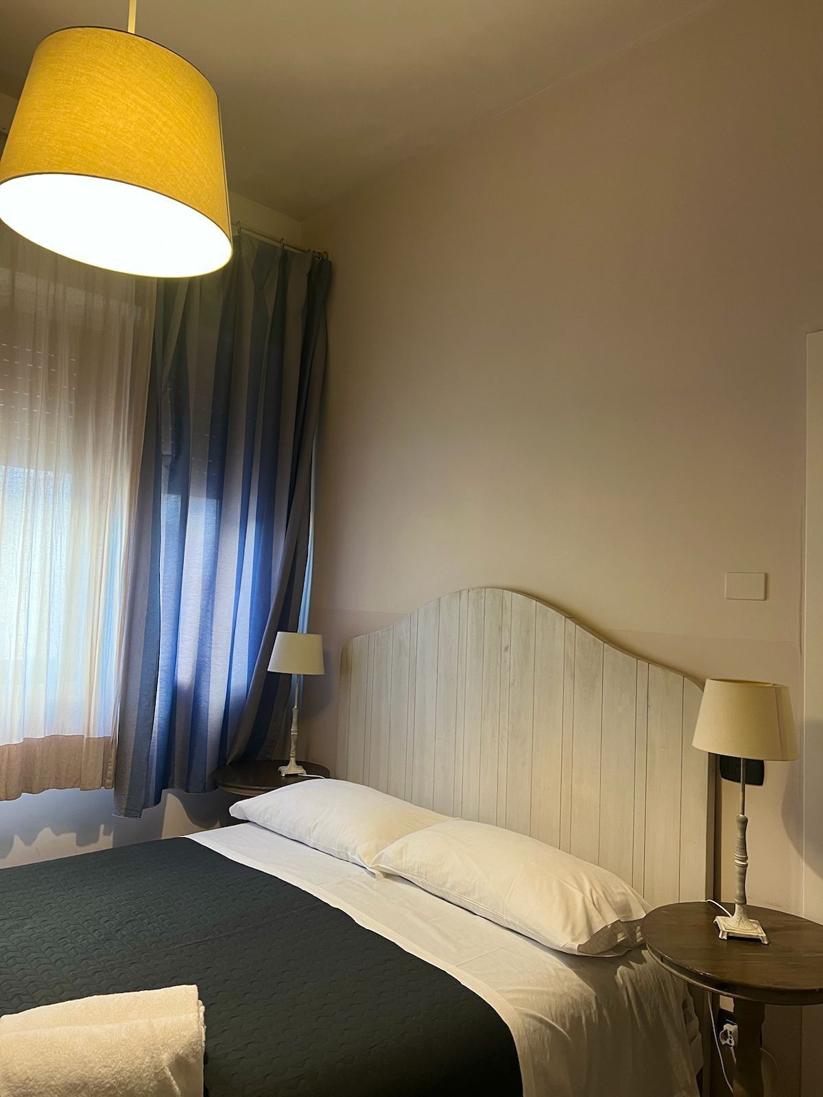 A hotel room with a bed, two bedside lamps, a window with curtains, and a wall-mounted light fixture.