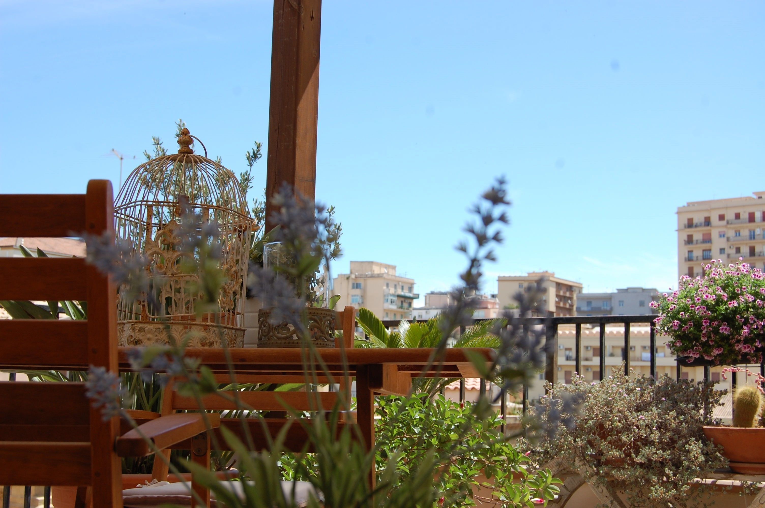 A balcony with a wooden chair, potted plants, and a view of buildings in the background.