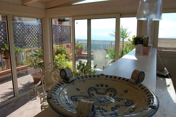 A sunlit patio with a large decorative bowl, a metal bench, and potted plants.