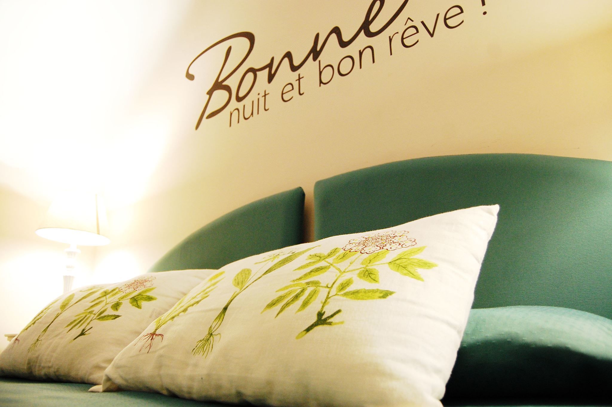 Una cama con cabecera verde y almohadas blancas con motivos florales.