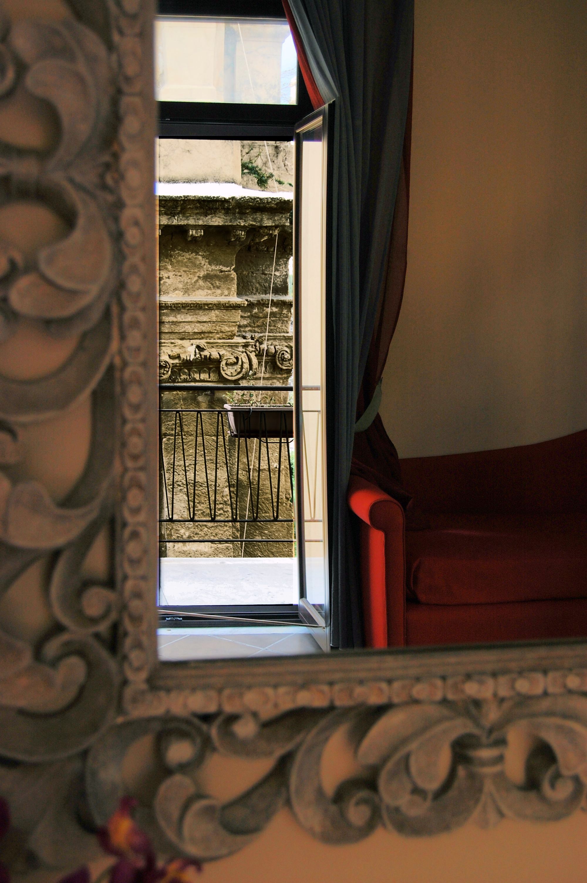 A room with a large ornate mirror reflecting a balcony with a metal railing and a chair.