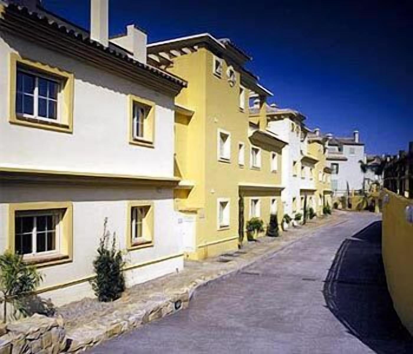 Une rangée de bâtiments jaunes dotés de balcons, une rue pavée et un ciel bleu azur.