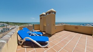 Terraço no telhado com duas poltronas azuis e vista para o mar.