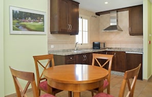 A kitchen with wooden cabinets, a granite countertop, a microwave, and a dining table with chairs.
