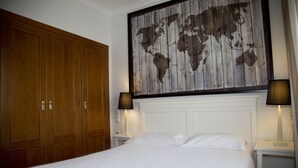 Quarto de hotel com um armário de madeira grande, cama com roupa de cama branca, duas luminárias de cabeceira e uma obra de arte com um mapa-múndi na parede.