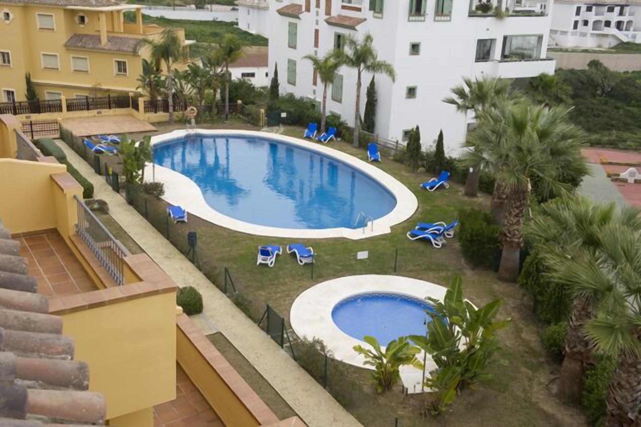 A swimming pool surrounded by lounge chairs and palm trees, with a view of residential buildings in the background.