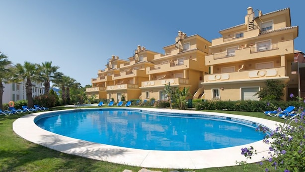 Hotel com piscina rodeada por espreguiçadeiras azuis.