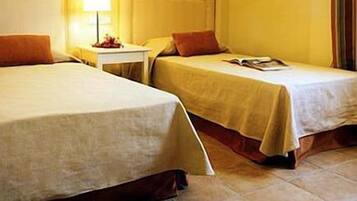 A hotel room with two beds, a nightstand, a lamp, and a window with curtains.
