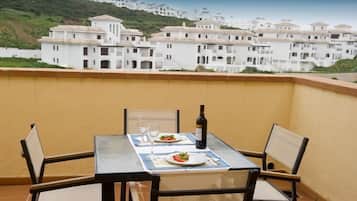 A balcony with a table set for two, a bottle of wine, and plates of food.
