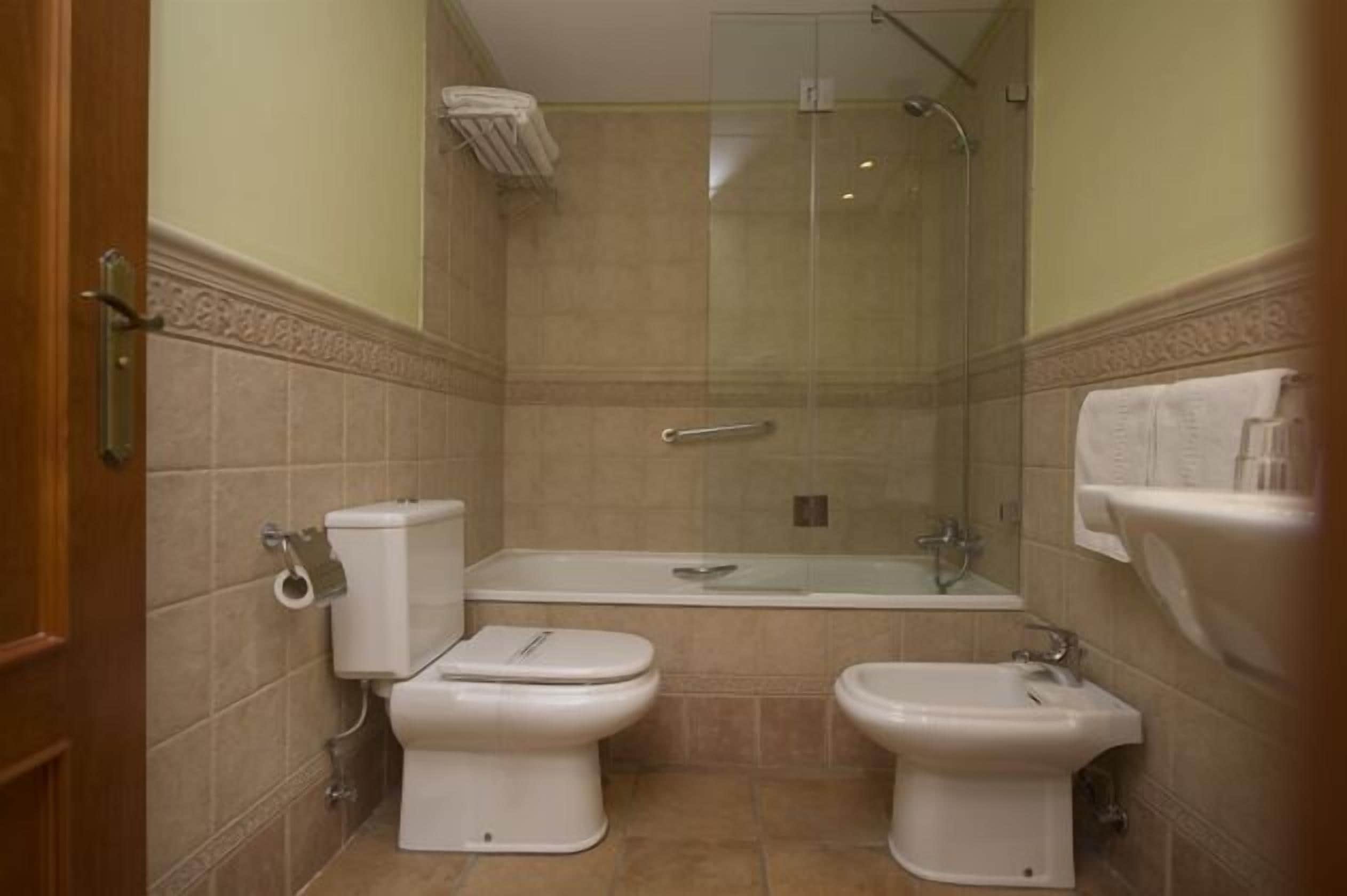 Un baño con inodoro, bidé, bañera y ducha con mampara de vidrio.