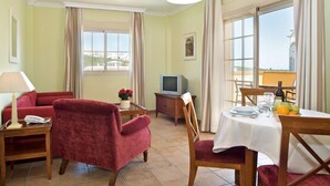 Quarto de hotel com área de refeições, televisão, sofá e vista para o mar.