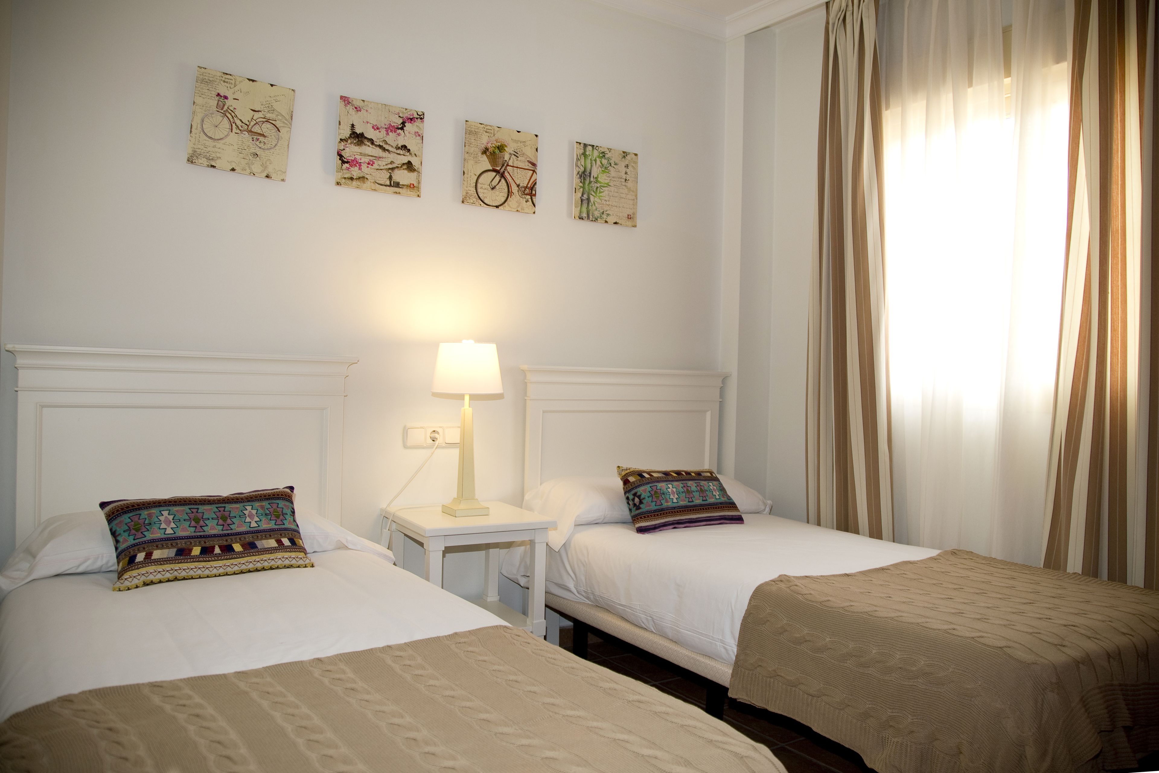 A hotel room with two beds, a nightstand with a lamp, and wall art depicting bicycles.