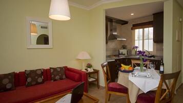 A compact living space with a red sofa, a dining table set for two, and a kitchenette in the background.