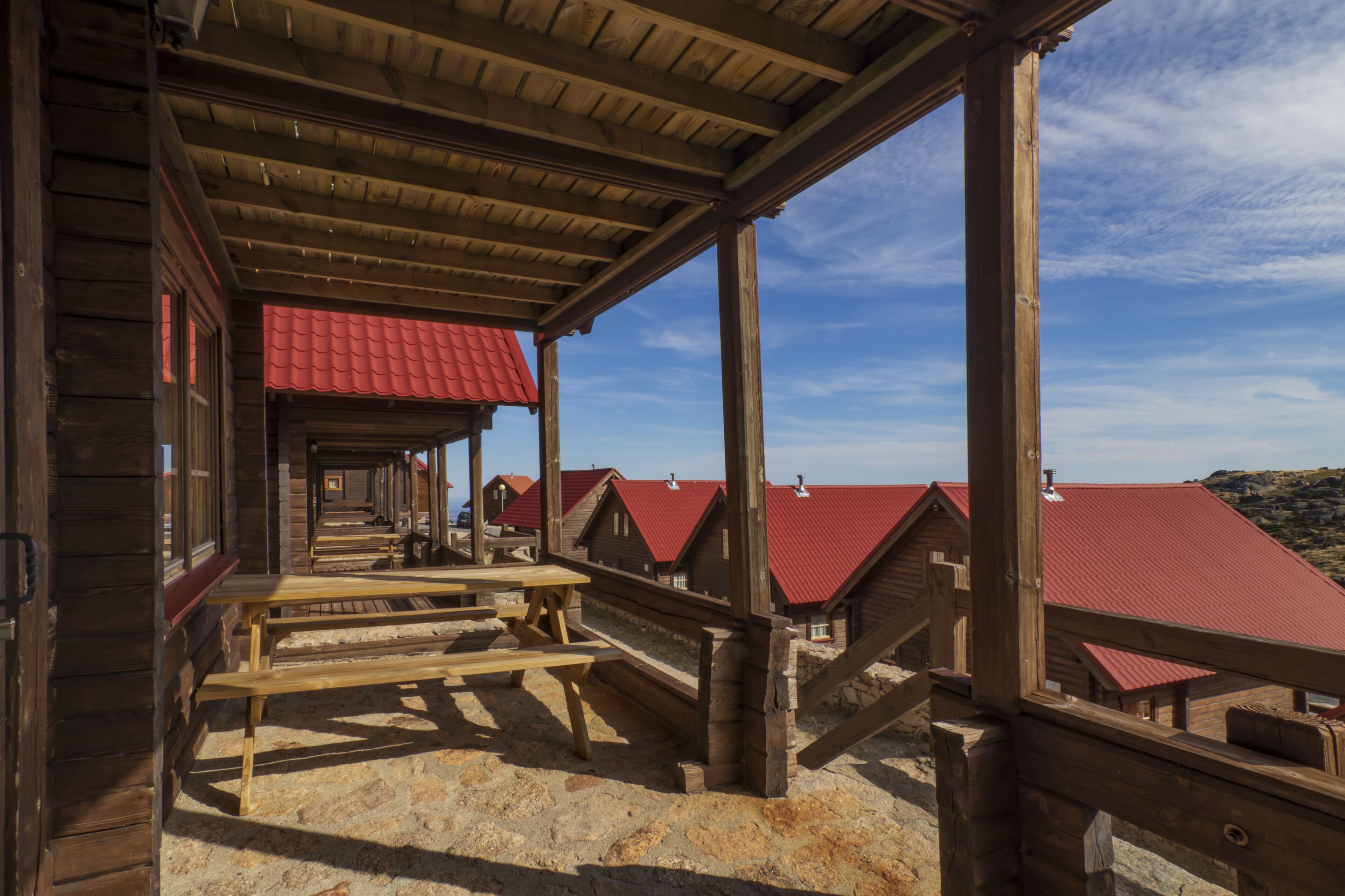 A wooden structure with a red roof, wooden benches, and a stone floor.