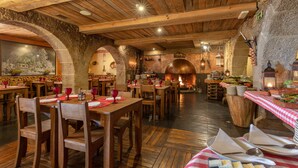 Een rustiek restaurant met houten tafels en stoelen, een stenen boog en een schouw van baksteen.