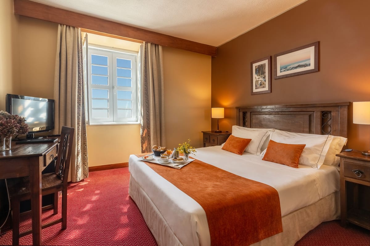 Hotelkamer met een groot bed, een bureau met televisie, een raam met gordijnen en een ontbijtservering op het bed.