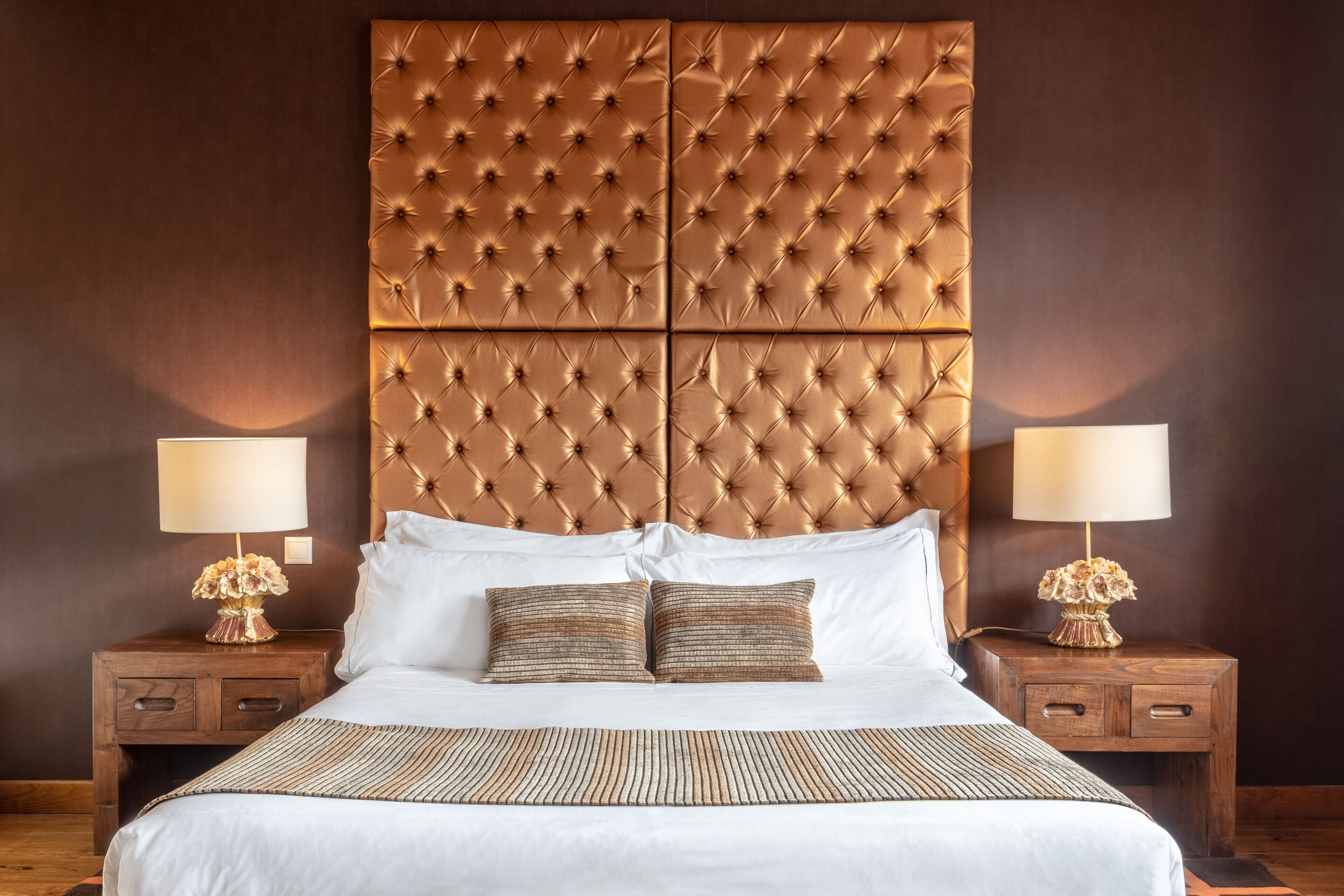 A large bed with a tufted headboard, white bedding, and two bedside tables with lamps and decorative vases.