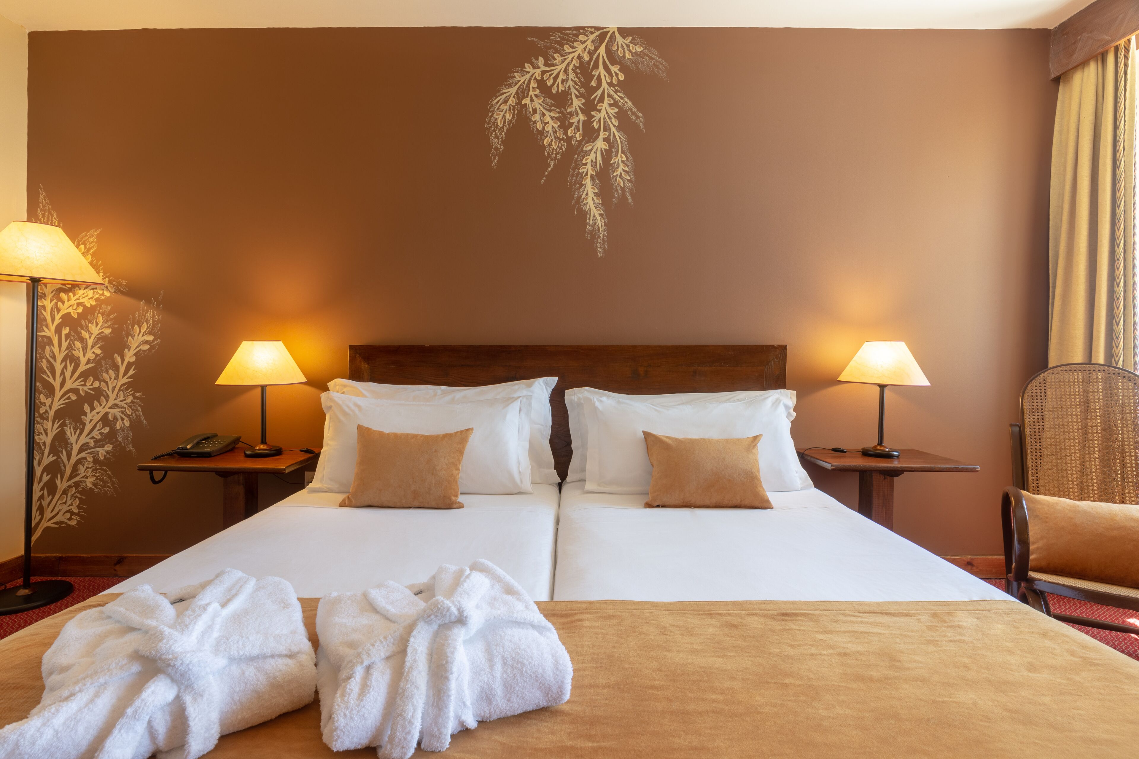 Habitación de hotel con cama doble, dos mesitas de noche con lámparas, una silla y dos toallas sobre la cama.