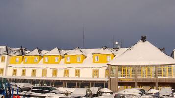 Un edificio con paredes exteriores amarillas y blancas, un letrero que dice "Recepção" y varios coches estacionados cubiertos de nieve.