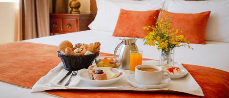 A neatly made breakfast tray with croissants, fruits, and coffee on a bed with orange bedding and pillows.