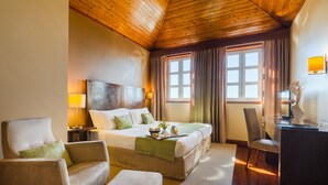 Een hotelkamer met een houten plafond, een groot bed met kussens, een bureau met lamp en een stoel.