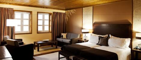 A hotel room with a wooden ceiling, a large bed with white linens, a sofa, a desk, and two lamps.