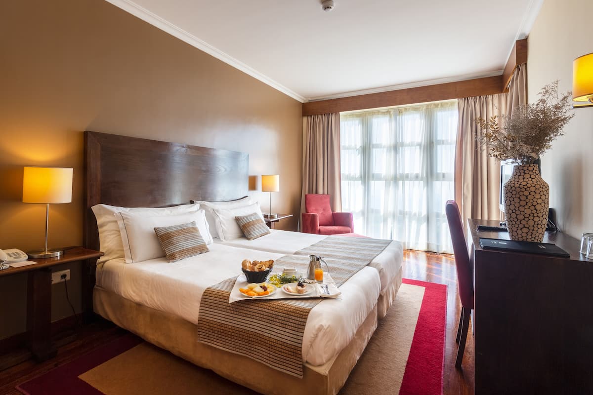 Hotelkamer met een groot bed, nachtkastjes, een bureau, een stoel en een raam met gordijnen.