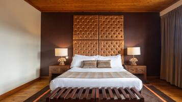 Un dormitorio ordenado con una cama grande, dos mesitas de noche con lámparas, un banco de madera y un cabecero capitonado.