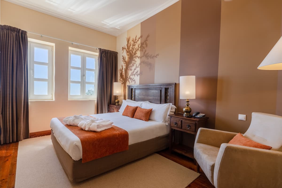 Een hotelkamer met een groot bed, nachtkastje, lamp en een stoel.