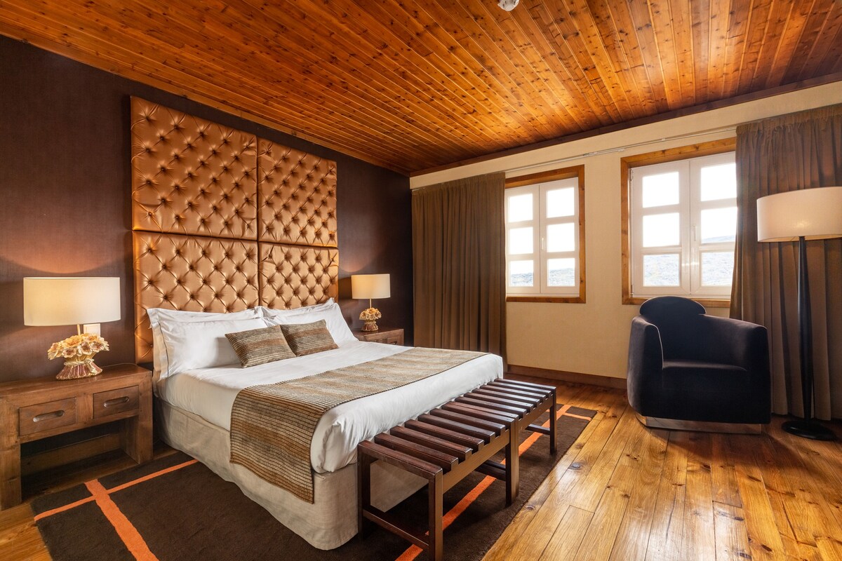 Una camera da letto con un letto grande, una testiera in legno, comodini con lampade, una panca e una sedia.