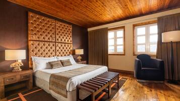 Un dormitorio con una cama grande, cabecera de madera, mesitas de noche con lámparas, un banco y una silla.