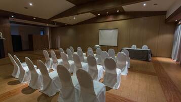 Uma sala de conferências com fileiras de cadeiras cobertas de branco, uma tela de projeção e uma mesa com um laptop.