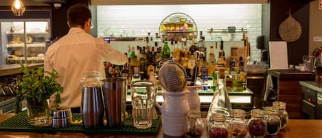 A bar area with a bartender preparing drinks, various bottles, and jars of spices on the counter.