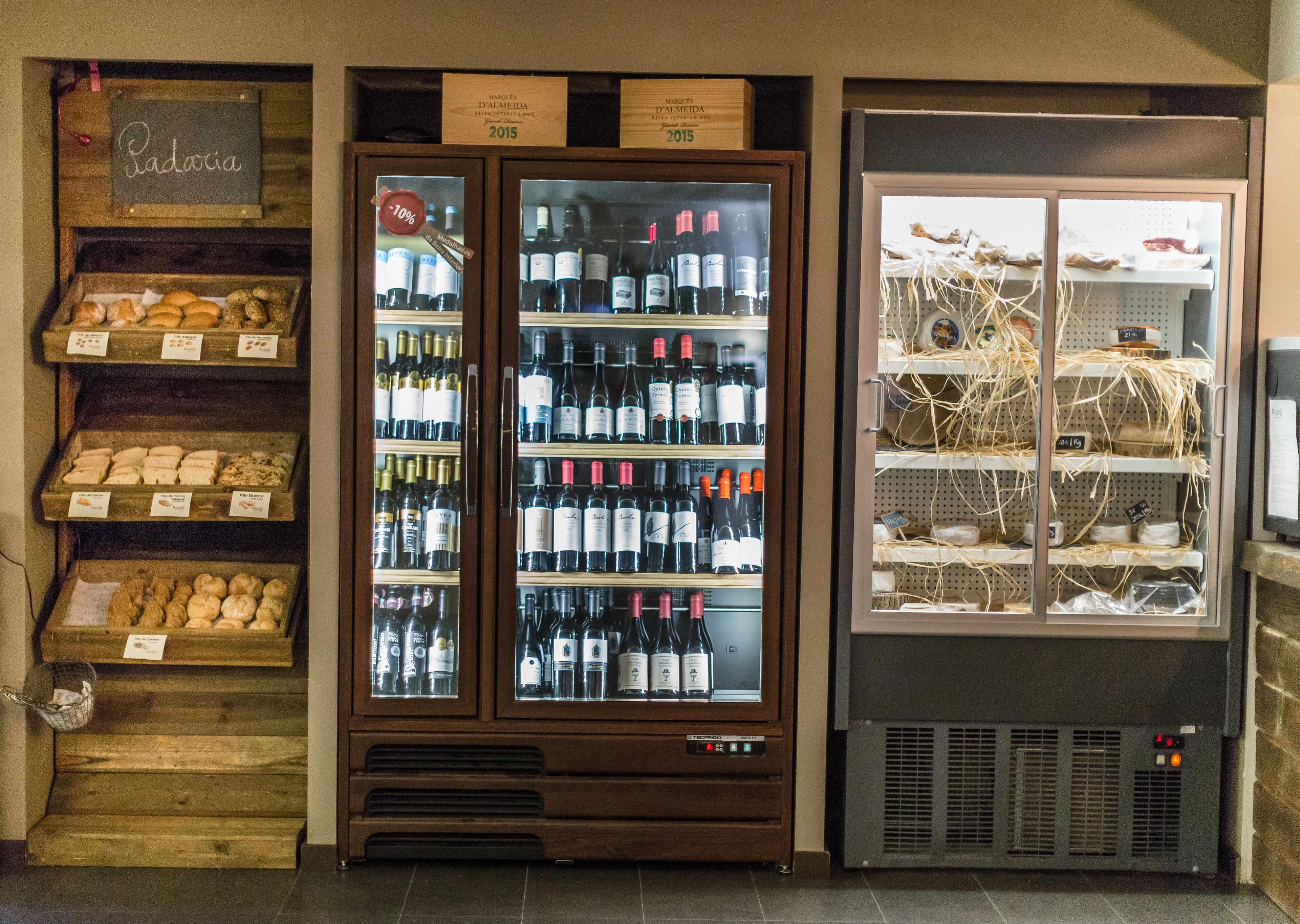 A wine cooler with multiple shelves of wine bottles, a display case with pastries, and a refrigerated display with various items.