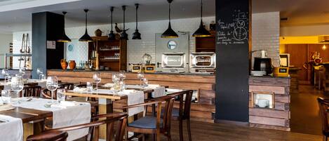 Un restaurante con mesas y sillas de madera, iluminación colgante y un menú en una pizarra.