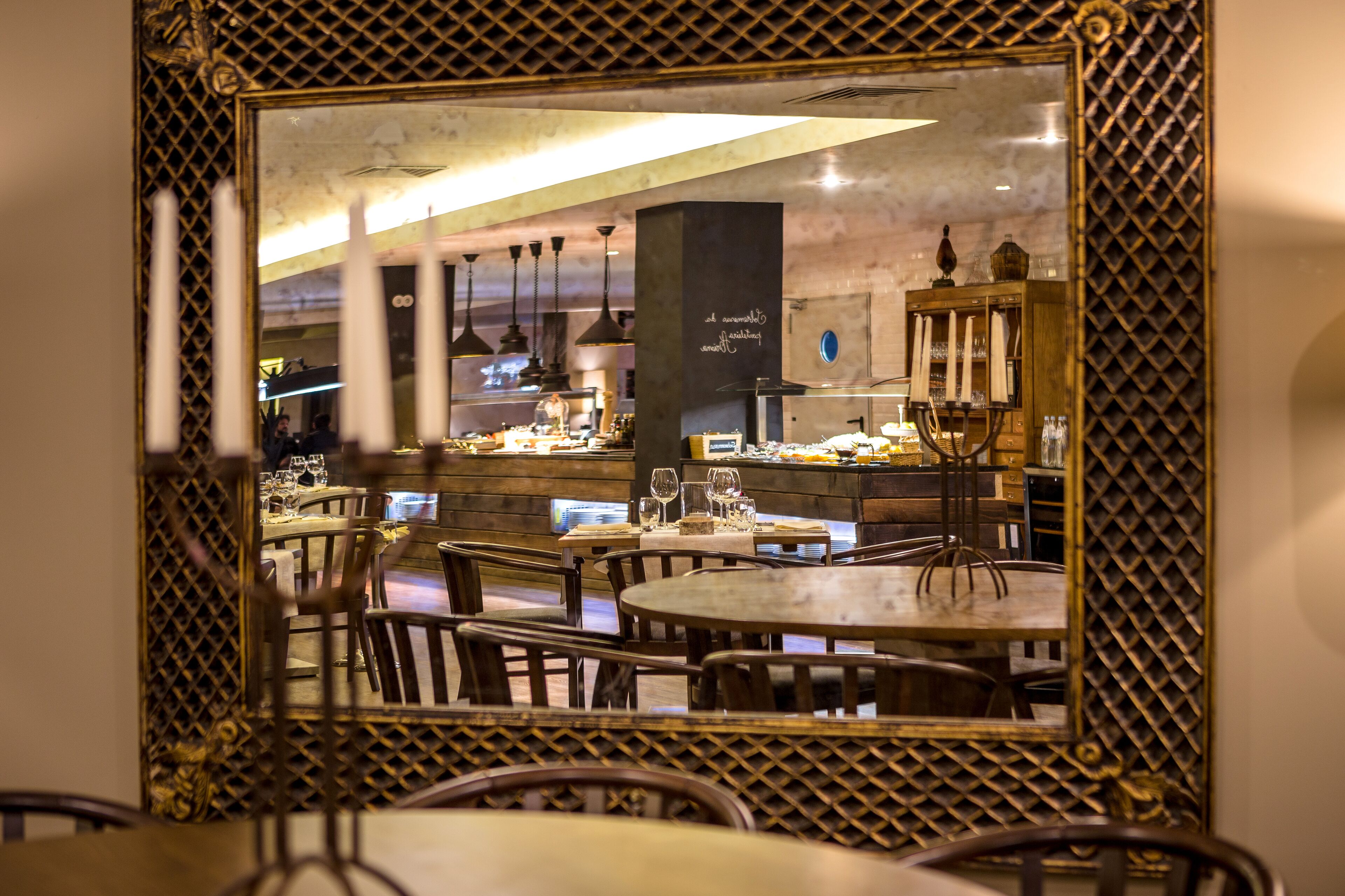 Un restaurante con mesas y sillas redondas, una zona de bar y un espejo grande con un marco decorativo.