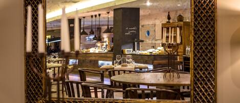 A restaurant with round tables and chairs, a bar area, and a large mirror with a decorative frame.