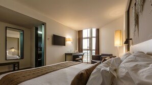 A hotel room with a large bed, a desk, a chair, a TV, and a window with curtains. - Puralã - Wool Valley Hotel & SPA (Covilhã)