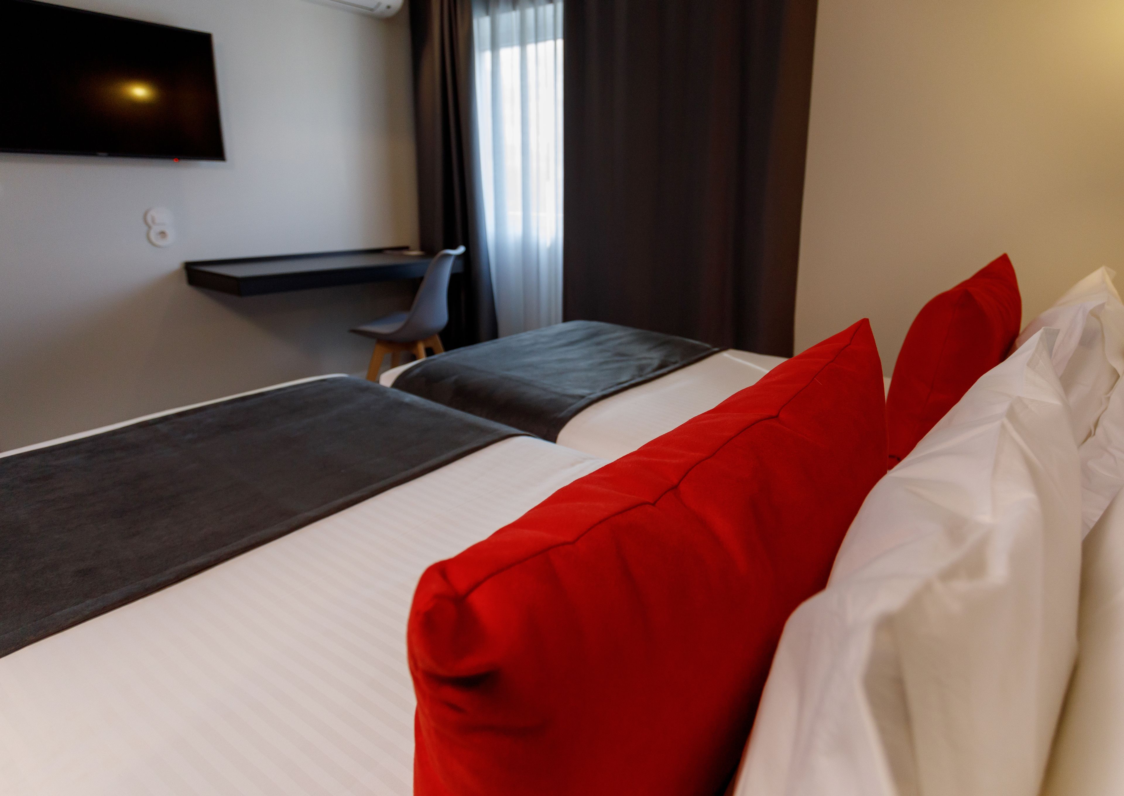 A hotel room with two beds, a TV mounted on the wall, a small table, and a chair.