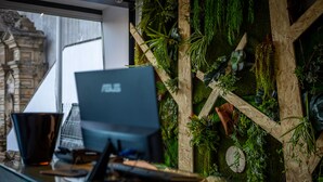 A desk with an ASUS laptop, a cup, and a keyboard. The desk is in front of a wall decorated with plants and wooden elements. - Sport Hotel Gym + SPA (Covilhã)
