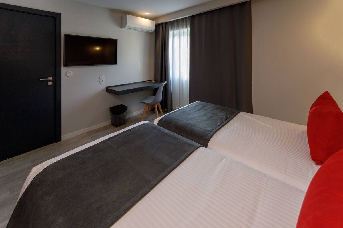 A hotel room with two beds, a desk, a chair, and a TV mounted on the wall.