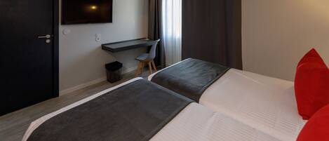A hotel room with two beds, a desk, a chair, and a TV mounted on the wall.