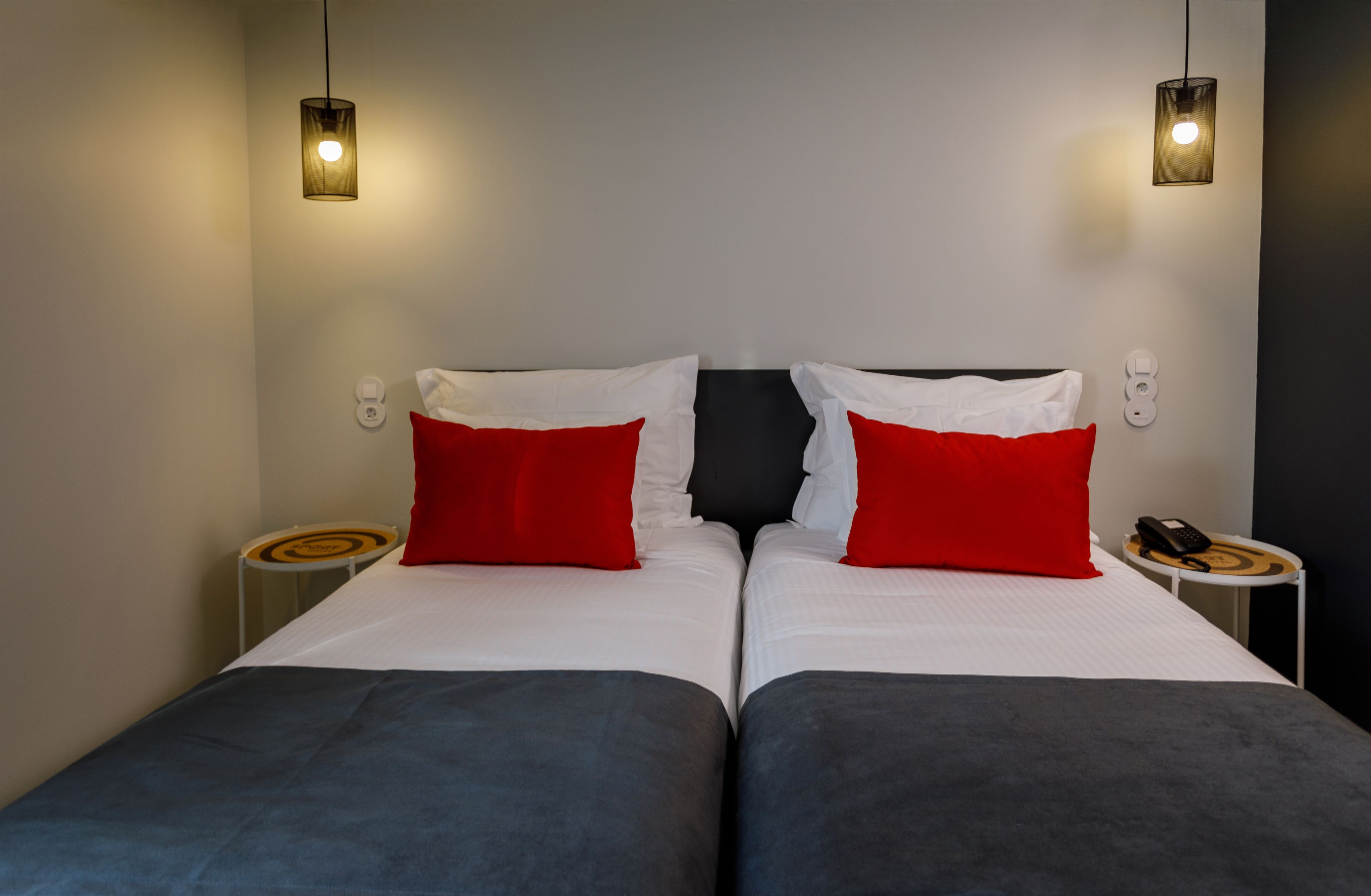 A double bed with white and red pillows, two bedside tables, and a phone on one table.