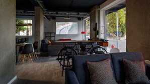 A modern living room with a large screen displaying a road map, a sofa, a dining table with chairs, and a bicycle. - Sport Hotel Gym + SPA (Covilhã)