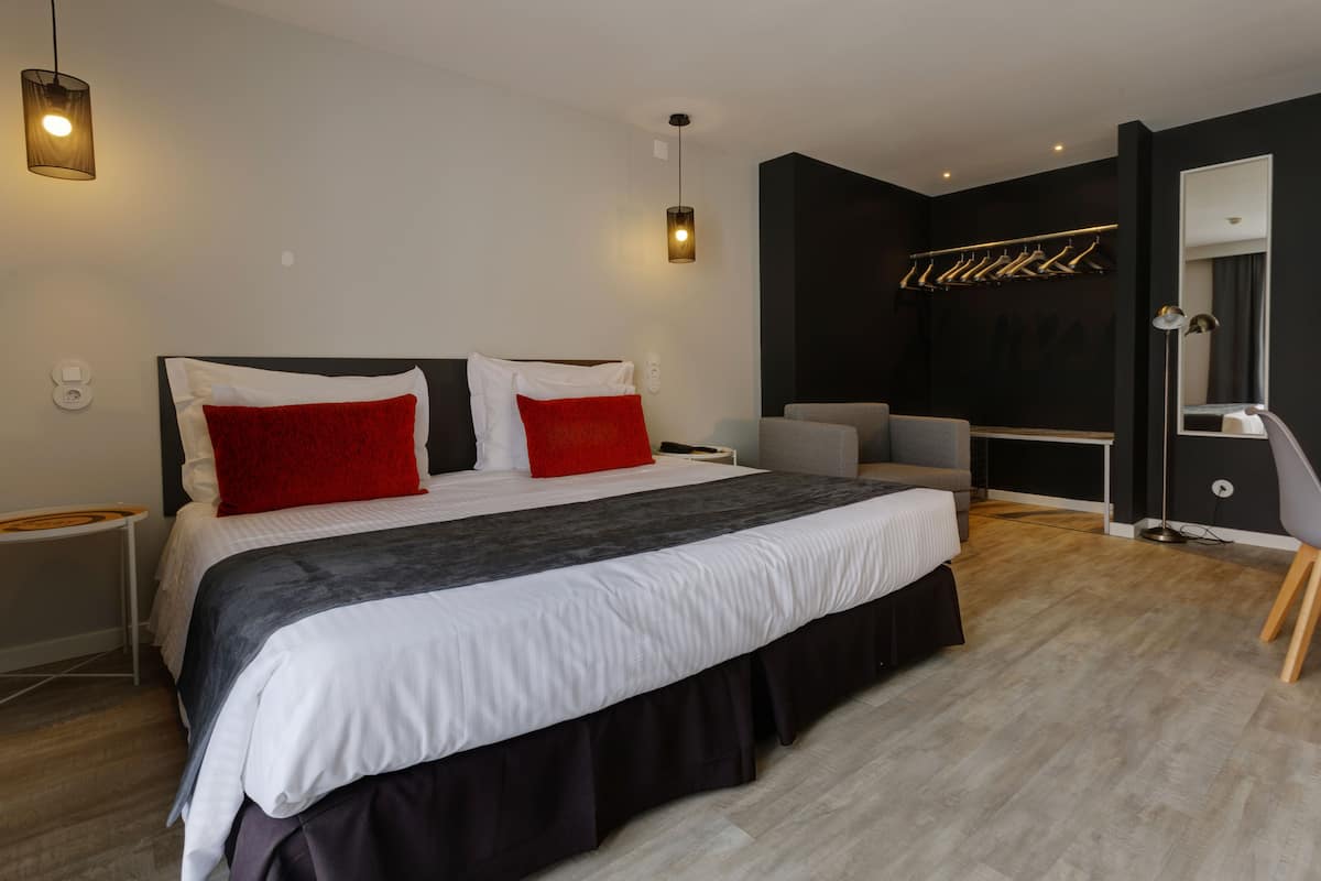A modern bedroom with a large bed, bedside tables, a desk, a chair, and a mirror.