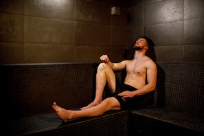 A person sitting on a bench in a room with tiled walls and a bench. - Sport Hotel Gym + SPA (Covilhã)